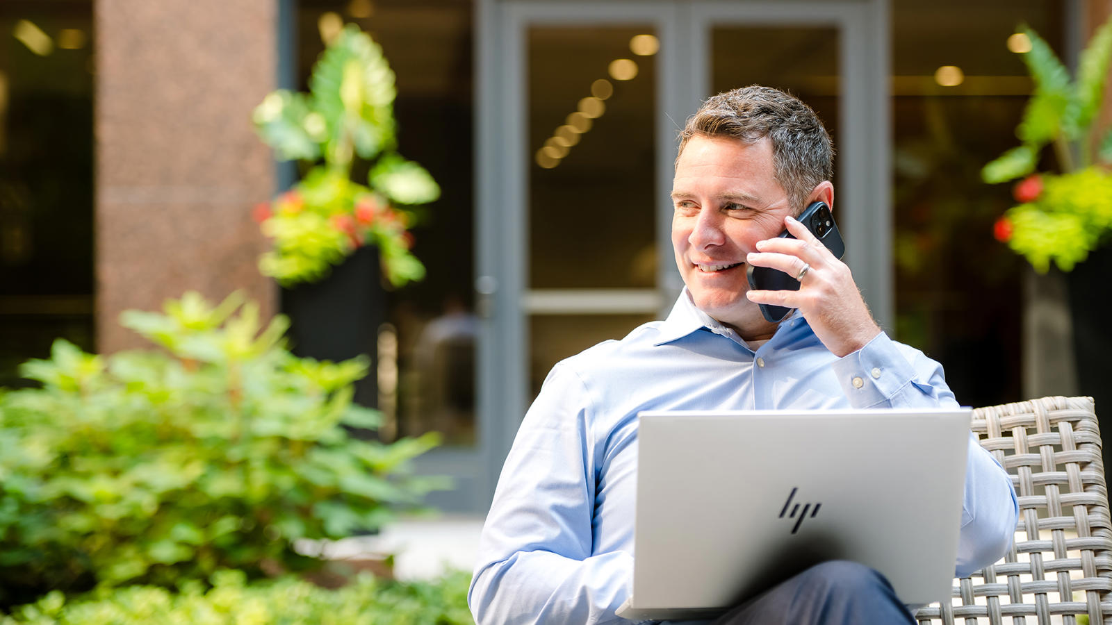 a person sitting outside talking on a cell phone and using a laptop