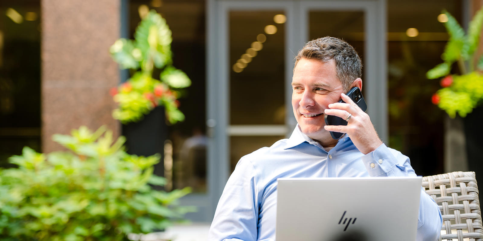 a person sitting outside talking on a cell phone and using a laptop